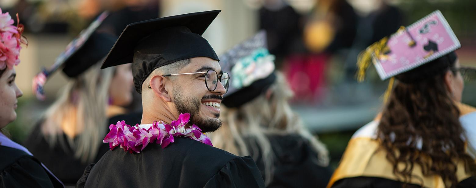 照片中，一名皇冠新现金网的毕业生戴着学士帽，穿着学士服，望着乌鸦. 